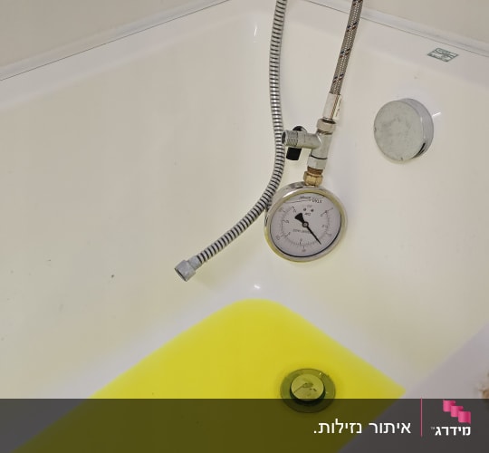 אמבטיה עם מים צהובים ומד לחץ, יד נראית בתמונה